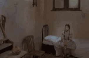 a girl is sitting on a bed in a room with a pumpkin on the floor .
