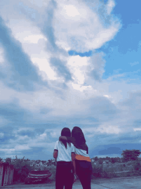 two girls hugging each other in front of a cloudy blue sky