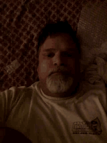 a man with a beard is laying on a bed wearing a white shirt that says fishing
