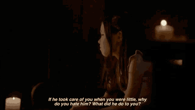 a little girl is talking to a man in a dark room with candles behind her