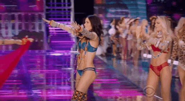 a group of women in bikinis are walking down a runway .