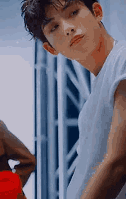 a young man in a white shirt is standing in front of a mirror and looking at the camera .