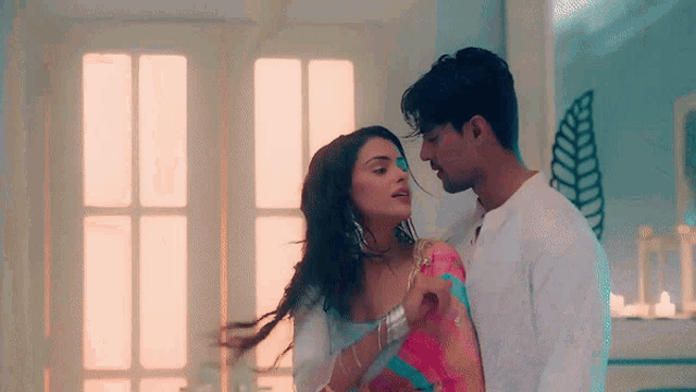 a man and a woman are kissing in a room . the woman is wearing a pink saree .