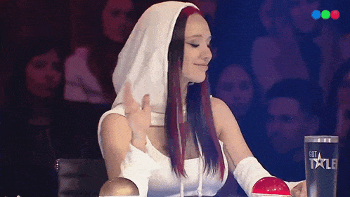a woman in a white hooded top is sitting in front of a glass that says got talent