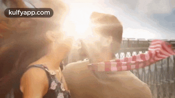 a man and a woman are kissing in front of a sun shining through the window .