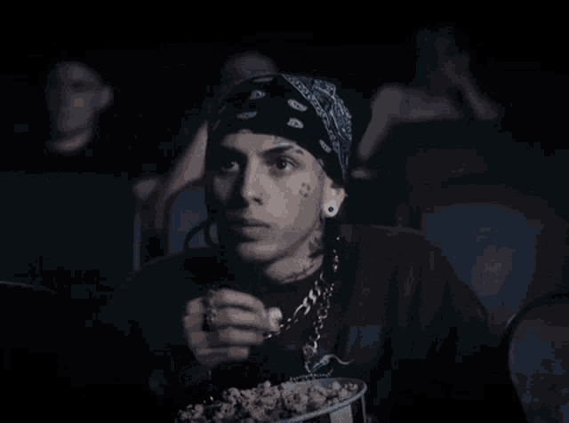 a man in a bandana is eating popcorn in a theater