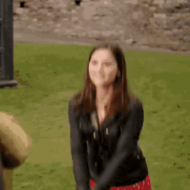 a woman in a red dress and a black jacket is clapping her hands in a park .
