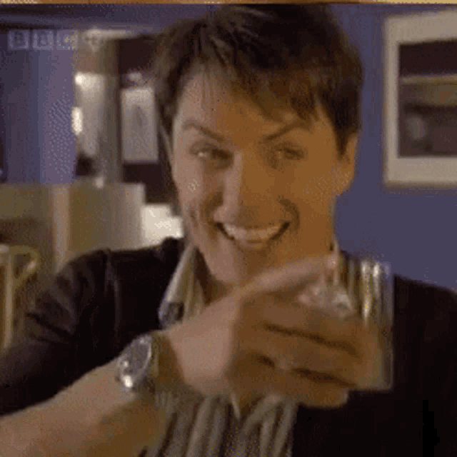 a man is smiling while holding a glass in front of a bbc sign