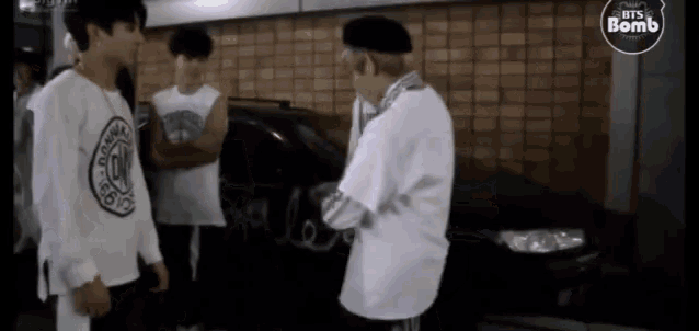 a group of young men are standing in front of a car and talking .