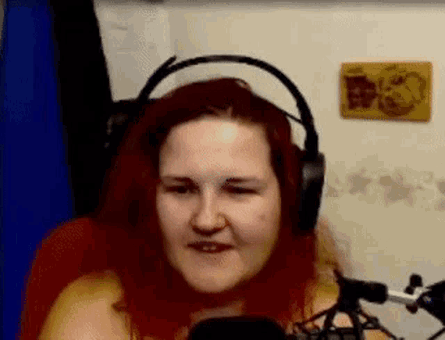 a woman wearing headphones is sitting in front of a microphone and making a funny face .