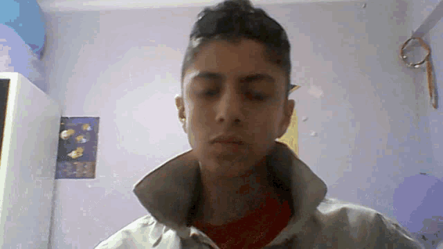 a young man looks at the camera with a poster on the wall behind him that says ' a '