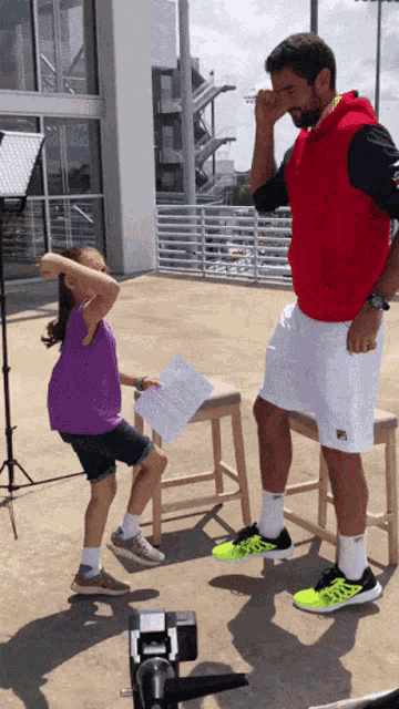 a man in a red hoodie is standing next to a little girl in a purple shirt