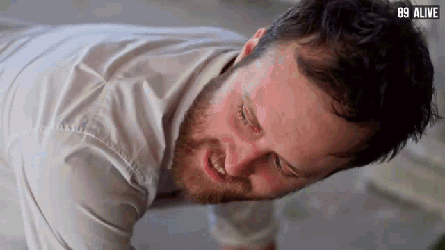 a man in a white shirt is laying on his back with the words 89 alive below him