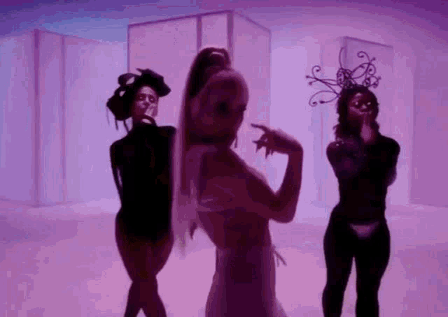 ariana grande is dancing with two other women in a purple room in a video .