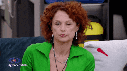 a woman with red curly hair is sitting on a couch with the words grandefratello on the bottom right