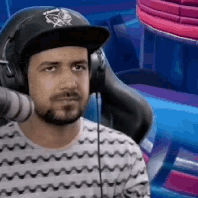 a man with a beard wearing headphones and a hat is sitting in a chair .