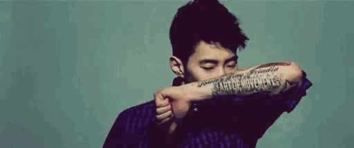 a man with a tattoo on his arm is holding his fist up in front of his face .