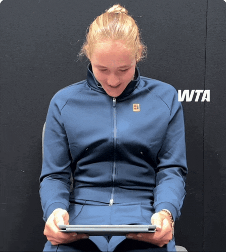 a woman sitting in front of a wall that has wta written on it
