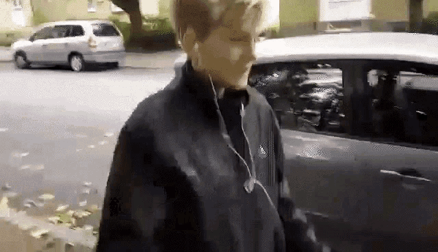 a man wearing ear buds is walking down a street next to a car .