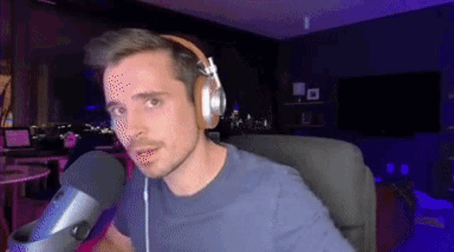 a man wearing headphones and a blue shirt is sitting in front of a microphone .