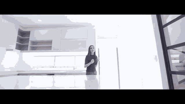 a woman in a black top is standing in a kitchen with white cabinets