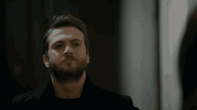 a man with a beard and a black coat looks at a woman