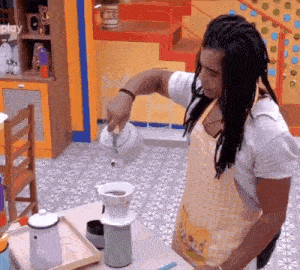 a man with dreadlocks is pouring coffee into a cup .