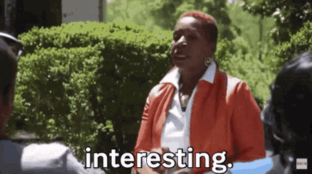 a woman in an orange jacket is talking to a man in a park and the woman is saying interesting .