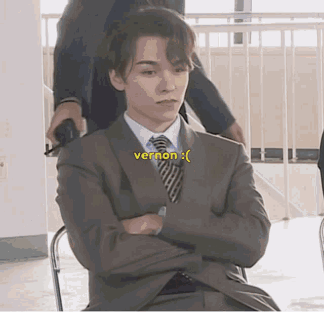 a man in a suit and tie is sitting in a chair with his arms crossed and the word vernon below him