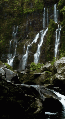 a waterfall is surrounded by rocks and trees and has a watermark on the bottom