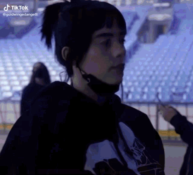 a woman wearing a mask and a ponytail is standing in a stadium .
