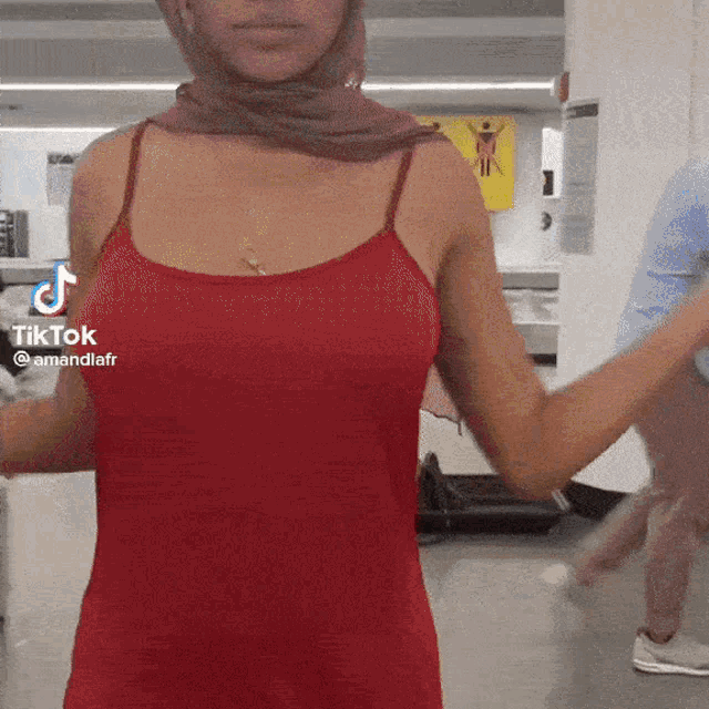 a woman wearing a red tank top and a hijab has tiktok written on her chest
