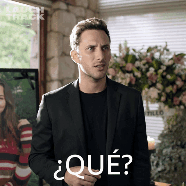 a man in a suit stands in front of a picture of a woman and says que