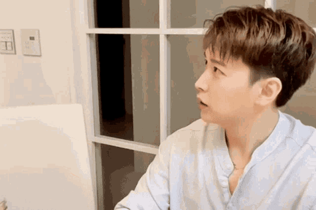 a young man is sitting at a table in front of a window looking at something .