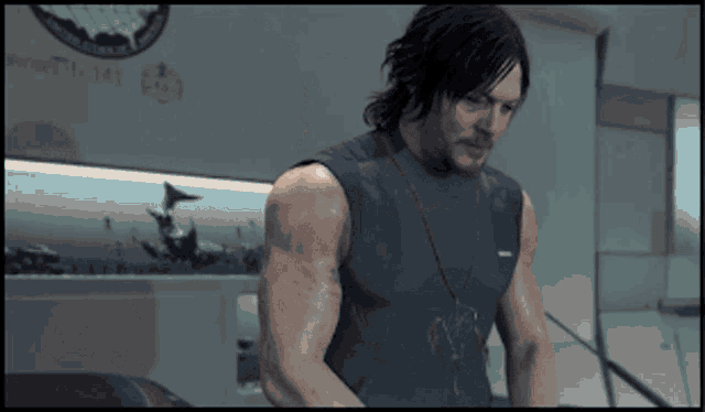 a man in a sleeveless shirt is standing in a room with a sign that says room 771 141