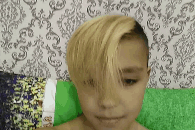 a young boy with blonde hair and a shaved head is laying on a bed .