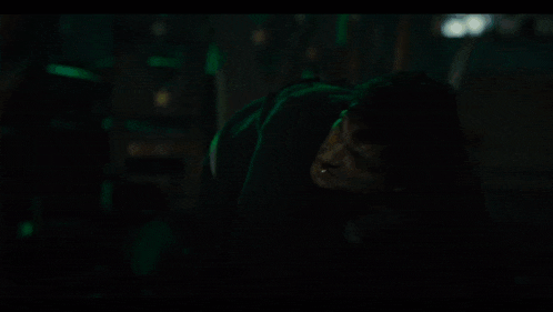 a man is standing in a dark room with a green light behind him .