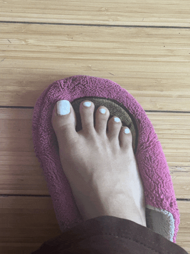 a woman 's foot in a pink slipper on a wood floor