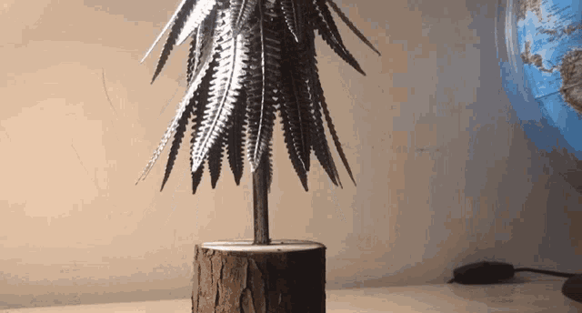 a tree made out of nails is sitting on a wooden stump next to a globe