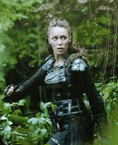 a woman in a samurai outfit is holding a sword in a forest .