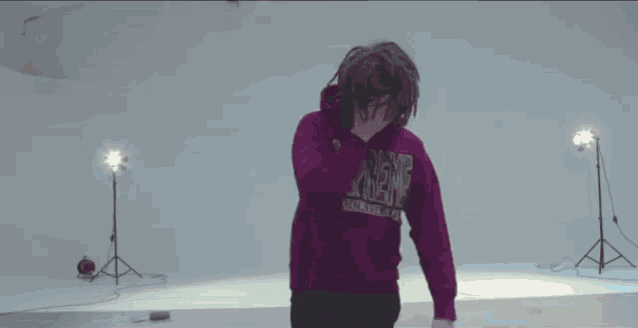 a man wearing a purple supreme hoodie is dancing in a room