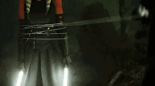 a person is tied up with a rope and holding two lightsabers in a dark room .