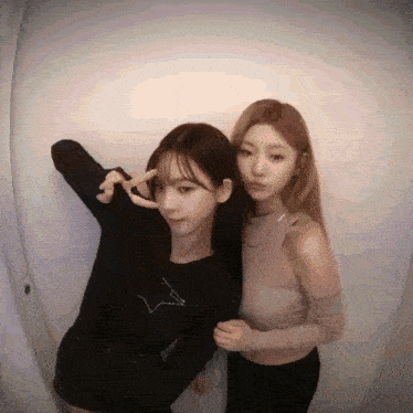 two girls are standing next to each other and making a peace sign with their hands .