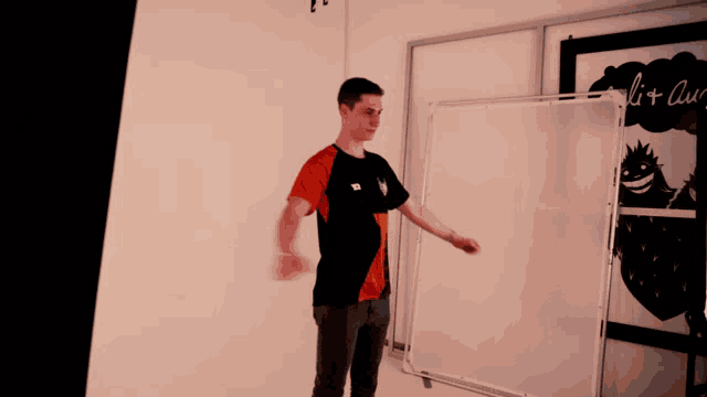 a man in an orange and black shirt stands in front of a white board that says " lit air " on it