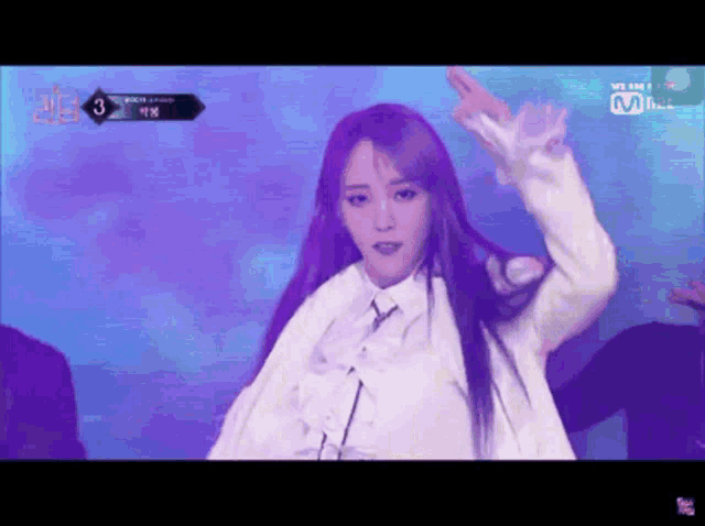 a woman with long purple hair is dancing on a stage with a mnet logo in the background