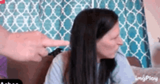 a woman is sitting on a couch with her hand pointing at her hair .
