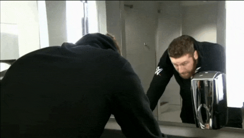 a man in a black hoodie looks at his reflection in a mirror