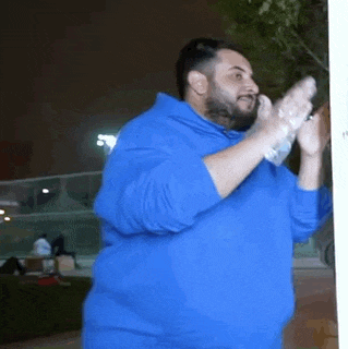 a man wearing gloves and a blue sweatshirt is standing in front of a window .