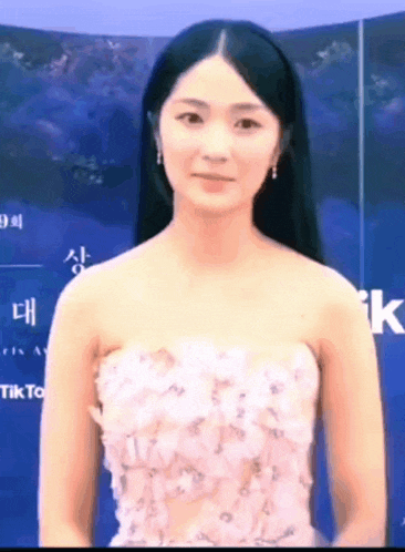 a woman in a strapless pink dress stands in front of a sign that says tiktok