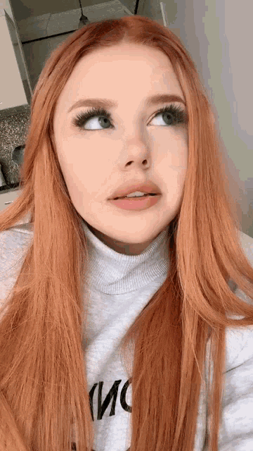 a woman with long red hair is wearing a grey sweater that says moschino on it